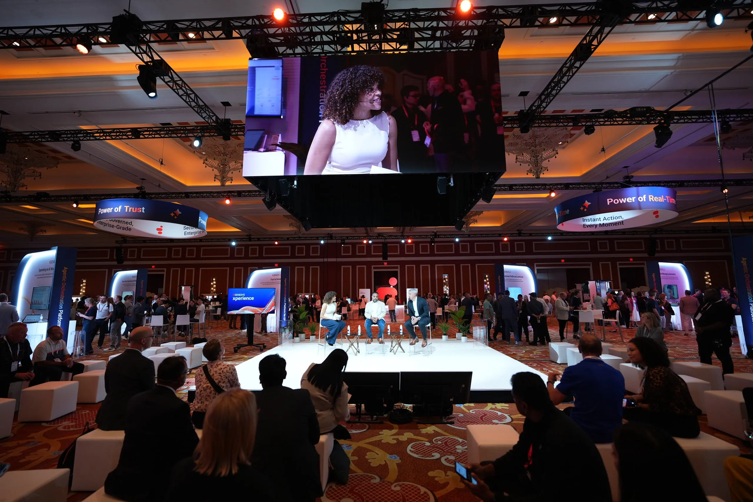 A packed conference ballroom: Marissa appears on a giant screen above the stage while she moderates a panel below, with the audience seated in the foreground.
